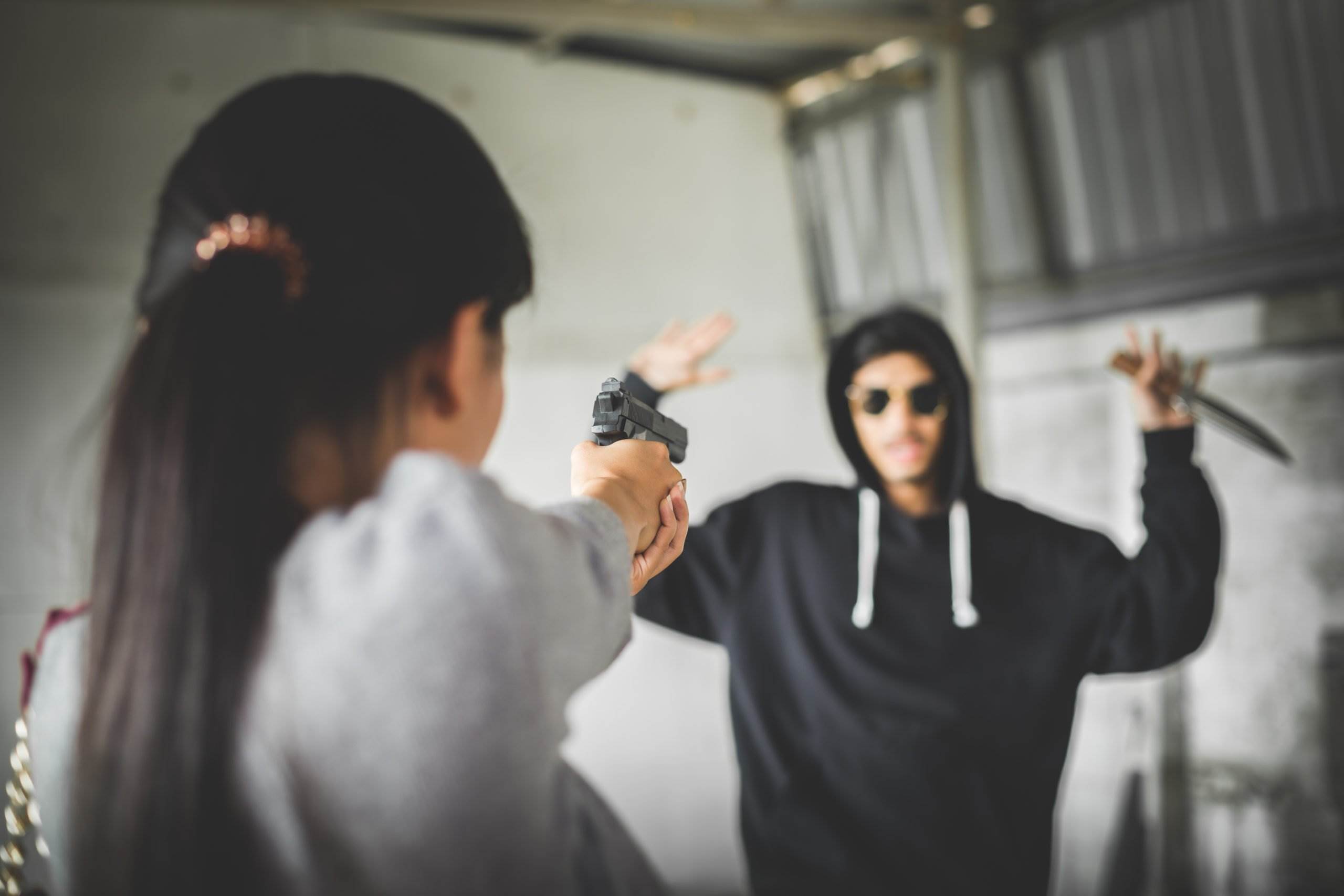 A woman pointing her gun at a man threatening her with a knife.