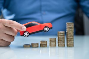 Hand holding toy car ascending piles of coins