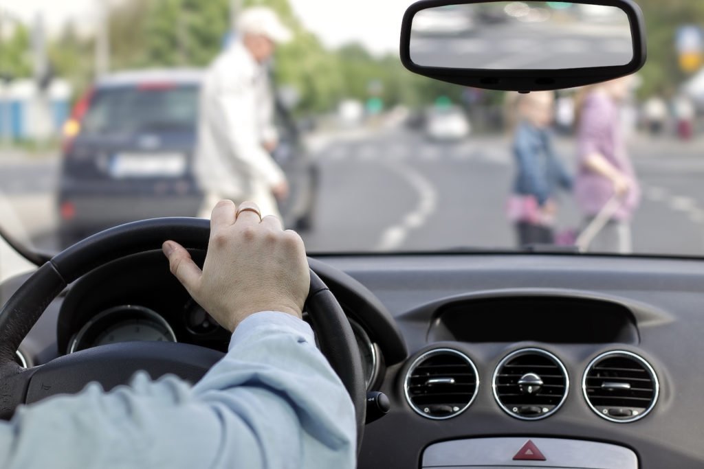 Closeup of driver's hand on wheel with pedestrians in view through the windshield