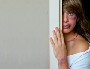 Battered woman cowering behind door