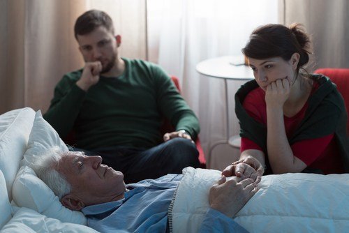 Concerned-looking adult siblings caring for their father, who is sick in bed, during kin care leave