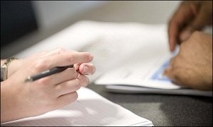 Closeup of two people's hands over a desk filling out insurance applications 