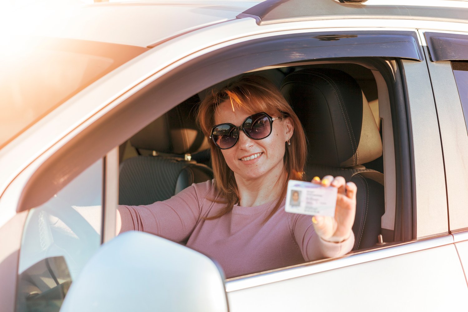 Woman in sedan holding up her driver's license after getting it reinstated by getting SR22 insurance