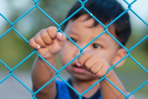 niño asiático detrás de una valla de alambre