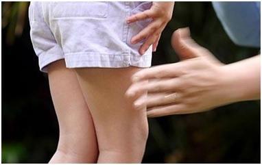 adult hand touching bare legs of a child in shorts