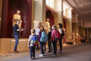 A group of school-children standing around their teacher at a museum.