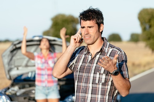 man on phone after car accident while angry woman in background is yelling at him