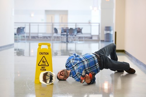 worker in hard hat lying on floor in pain next to wet floor placard
