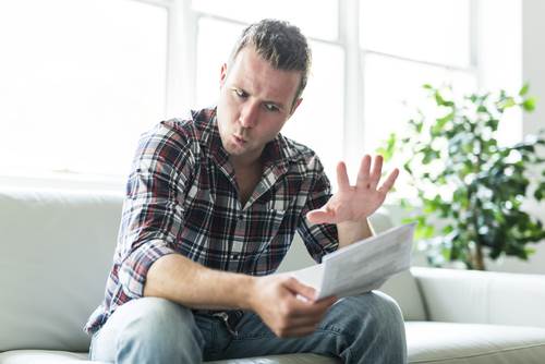 man appearing surprised and upset as he looks at an invoice