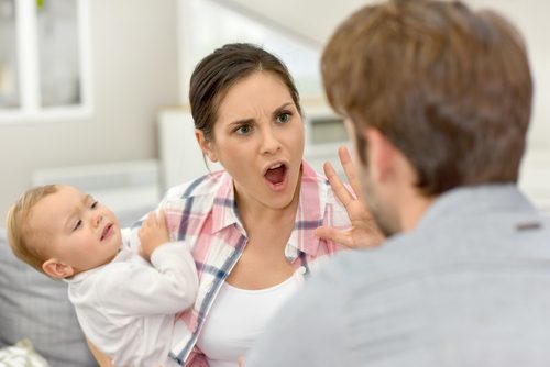 Mujer sosteniendo a un bebé y levantando la palma de la mano durante una discusión con el padre del bebé