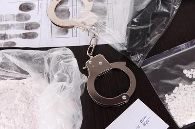 Handcuffs, fingerprints, and piles of drugs placed on top of a table