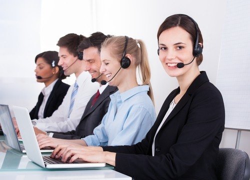cinco recepcionistas con auriculares en un centro de llamadas