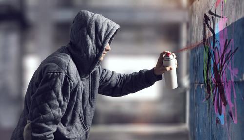 hooded man spray painting graffiti - civil compromise is common in low-level vandalism cases