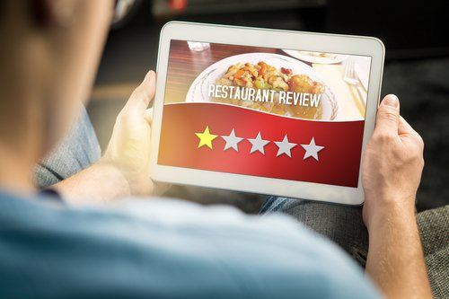 Hombre sosteniendo una tableta a punto de dejar una reseña de una estrella de un restaurante para ilustrar la difamación comercial