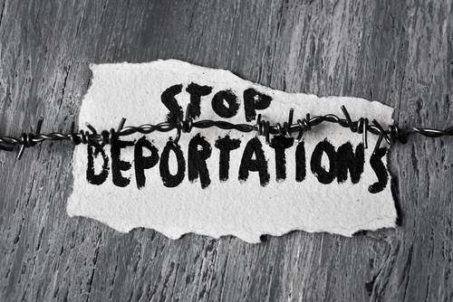 Mano pintada señal leyendo "detener las deportaciones" sostenida en un pedazo de madera por alambre de púas
