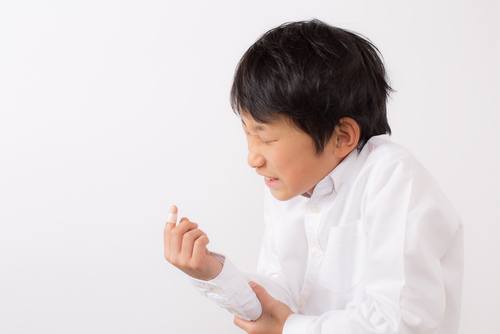 child in white shirt wincing and clutching his lower arm