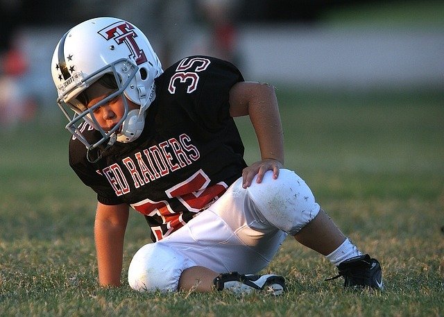 young football player in uniform on ground looking dazed