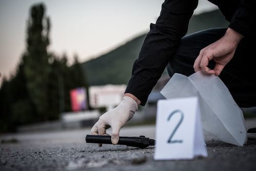 Oficial forense en una escena del crimen recogiendo un arma con una mano con guantes para ponerla en una bolsa de evidencia