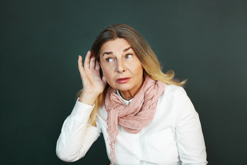 una mujer con la mano detrás de la oreja como si escuchara - el oídas generalmente es inadmisible en los procedimientos judiciales de California según el Código de Evidencia 1200