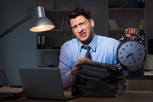 Hombre sobrecargado detrás de un escritorio sosteniendo un reloj