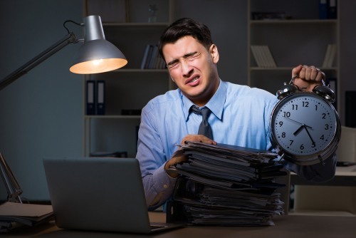 Overworked man behind a desk holding a clock