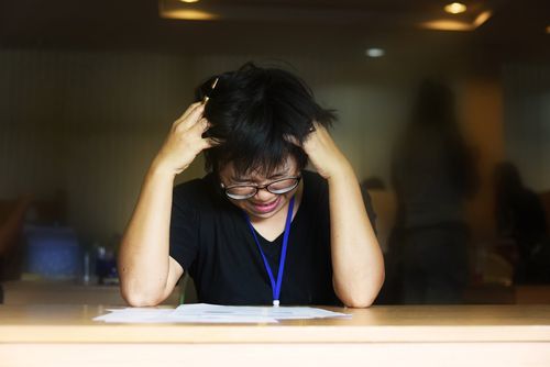 Una joven asiática sosteniendo sus manos en su cabeza y frunciendo el ceño mientras intenta trabajar en un documento
