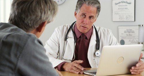 Médico mayor mirando la computadora portátil mientras habla con el paciente - muchos médicos tratarán a las víctimas de accidentes tomando un gravamen médico en su caso