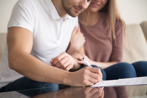 una joven pareja sonriendo y firmando un acuerdo