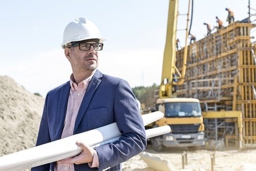 contratista sosteniendo esquemas frente a un sitio de construcción