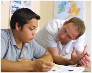 maestro masculino inclinándose sobre el escritorio en el que un joven estudiante masculino está sentado