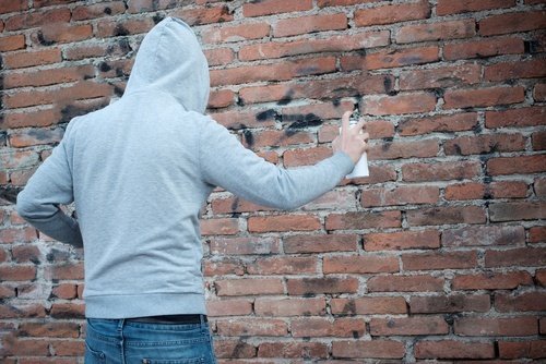 Young man in hoodie spray painting graffiti onto a brick wall