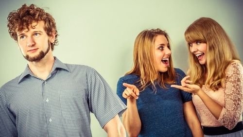 two women whispering and pointing at young man