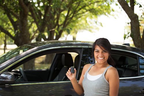 una mujer latina feliz sosteniendo una llave frente a un auto
