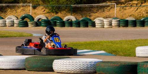 Child in helmet riding a go-kart on on a track lined with tires lying on their sides