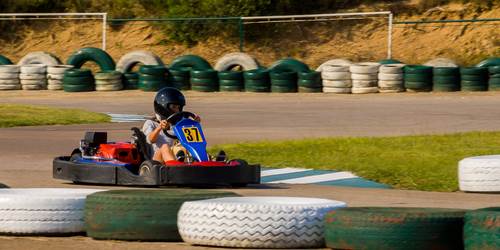 Niño con casco montando un go-kart en una pista bordeada con neumáticos tendidos de lado