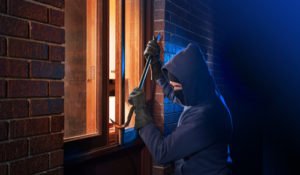 Hooded man trying to break in window at night