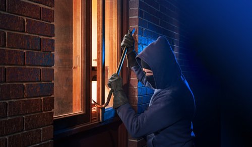 Hooded man trying to break in window at night