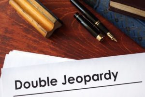 Paper that says "double jeopardy" on a desk along with books and a pen