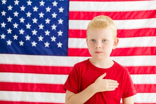 young boy in front of U.S. flag with hand over heart