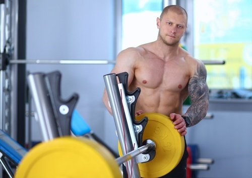 buff shirtless man changing free weights on bench press