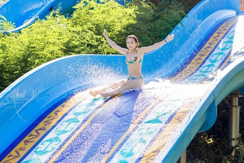 girl riding raft down water slide with her hands in the air