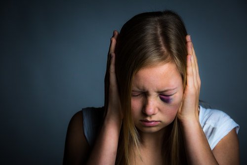 niña traumatizada con un ojo morado sosteniendo sus manos sobre sus oídos contra un fondo oscuro