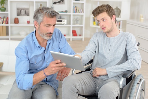 bearded man holding up laptop computer for young man in wheelchair as an example of where a life care plan may come into play