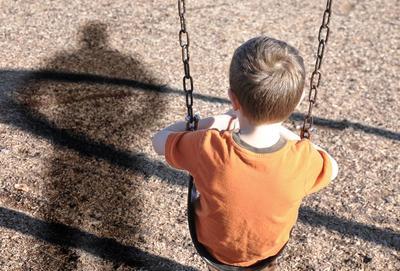 niño sentado en un columpio con una sombra adulta junto a él