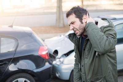 hombre sosteniendo la parte posterior de su cabeza frente a dos autos que han chocado