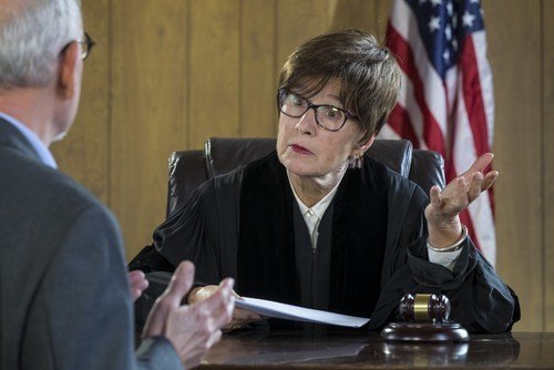 female judge behind bench listening to argument of older male lawyer