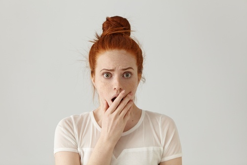 young woman holding hand over her mouth in shock