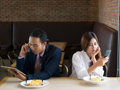 Pareja asiática en restaurante, mirando en direcciones opuestas y hablando en sus teléfonos celulares