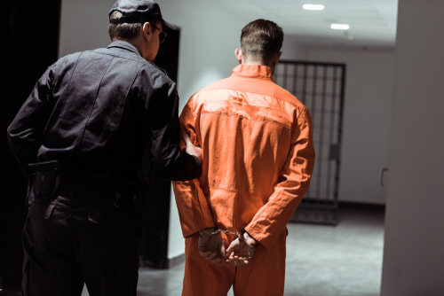 inmate in orange jumpsuit being taken to a jail cell by a warden following a conspiracy conviction