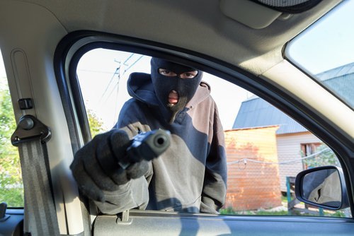 Hombre enmascarado apuntando con un arma a un auto como ejemplo de un robo de autos según el Código Penal 215 PC